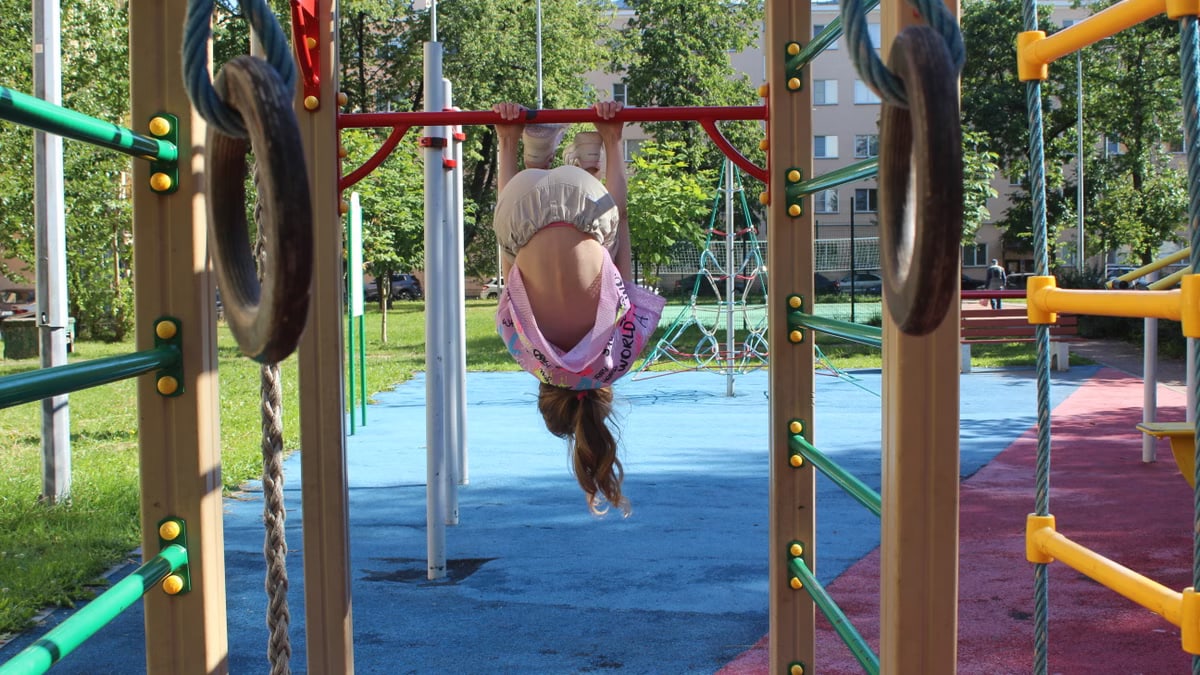 Girl having fun hanging upside down on monkey bars at sunny playground.
